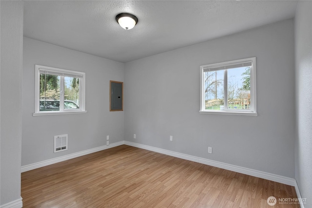 spare room featuring electric panel, a healthy amount of sunlight, visible vents, and light wood finished floors