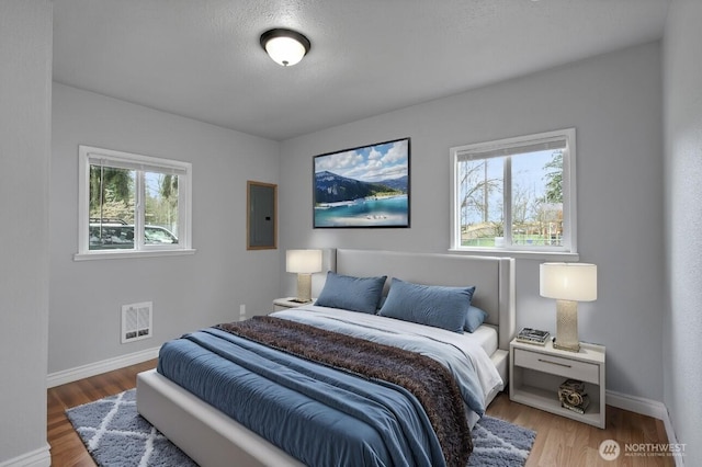 bedroom featuring electric panel, visible vents, baseboards, and wood finished floors