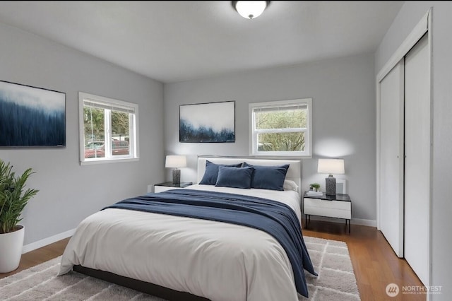 bedroom with a closet, multiple windows, baseboards, and wood finished floors