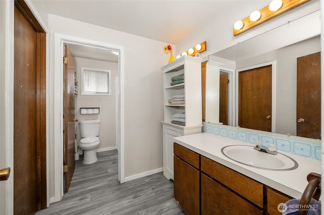 bathroom with toilet, vanity, baseboards, and wood finished floors