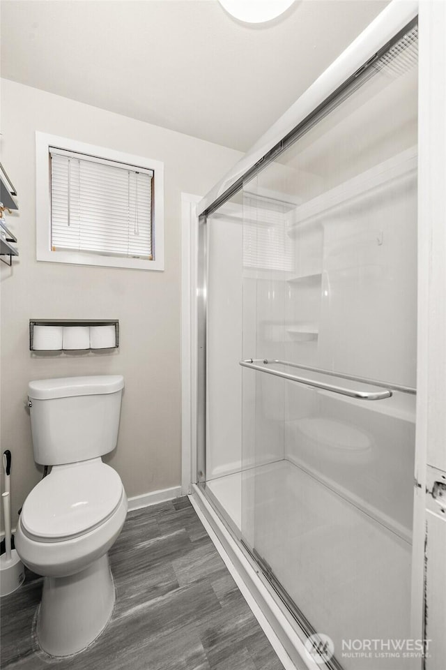 bathroom with a shower stall, toilet, wood finished floors, and baseboards