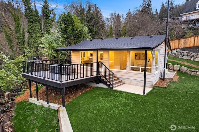 view of front of property featuring a front lawn, fence, a wooden deck, roof with shingles, and a patio