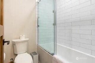 bathroom featuring enclosed tub / shower combo and toilet