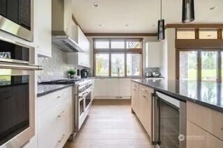 kitchen featuring beverage cooler, dark countertops, tasteful backsplash, appliances with stainless steel finishes, and wall chimney exhaust hood