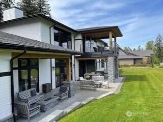 rear view of house featuring a patio area, a balcony, a lawn, and a chimney