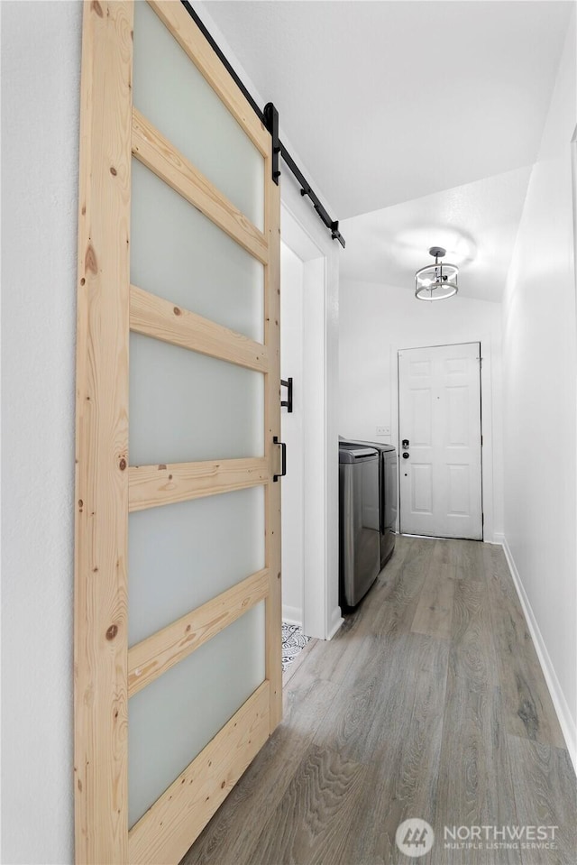 hallway featuring washer and dryer, baseboards, a barn door, and wood finished floors