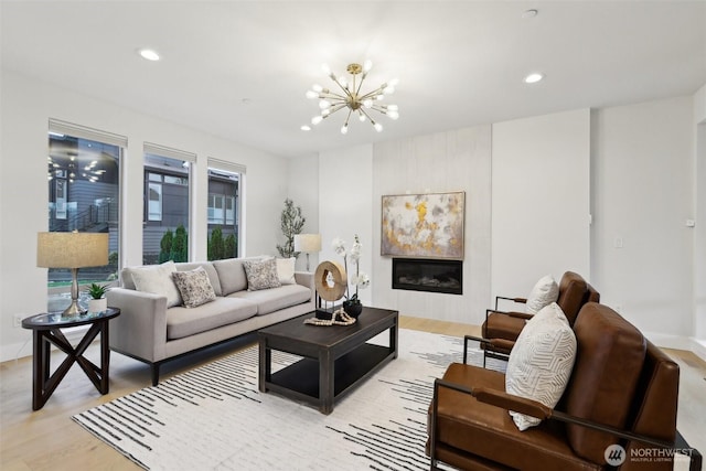 living room featuring recessed lighting, a notable chandelier, a glass covered fireplace, and light wood finished floors