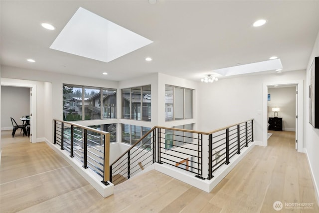 hallway with an upstairs landing, a skylight, and wood finished floors