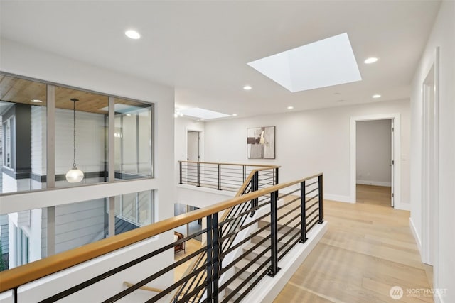 hall featuring an upstairs landing, recessed lighting, a skylight, light wood finished floors, and baseboards