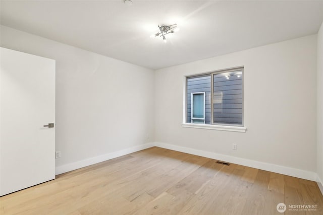 empty room with wood finished floors, visible vents, and baseboards