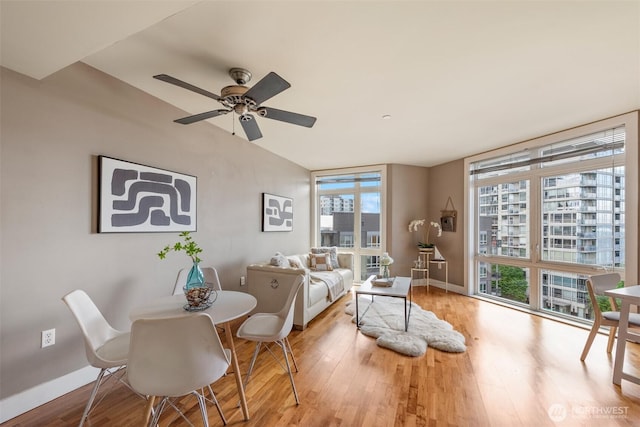 living room featuring ceiling fan, baseboards, wood finished floors, and floor to ceiling windows