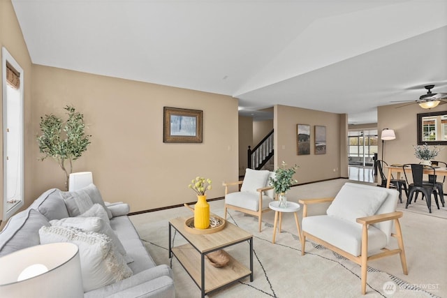 living area with light carpet, a ceiling fan, stairway, baseboards, and vaulted ceiling