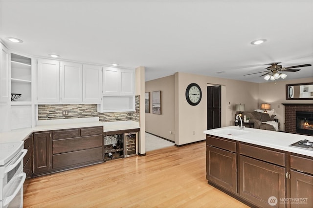 kitchen with light wood-type flooring, beverage cooler, open shelves, a sink, and a brick fireplace