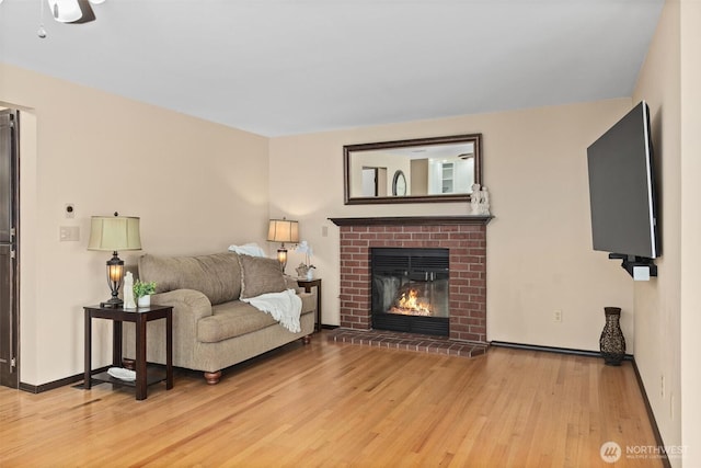 living area featuring light wood-style flooring, a fireplace, baseboards, and ceiling fan