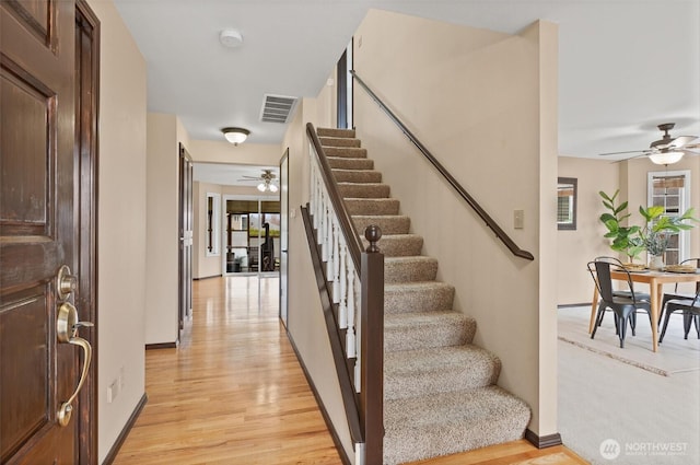 stairs featuring a healthy amount of sunlight, wood finished floors, visible vents, and ceiling fan