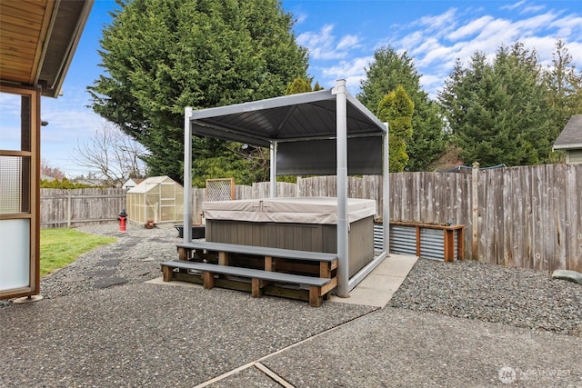 view of patio / terrace with a hot tub, a gazebo, a storage shed, a fenced backyard, and an outdoor structure