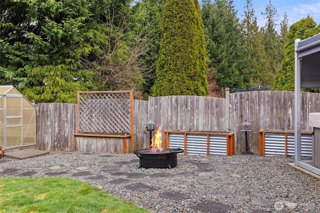 view of yard featuring a greenhouse, an outdoor structure, a fenced backyard, and an outdoor fire pit