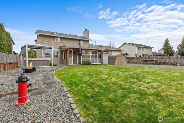 back of property featuring a fenced backyard, a sunroom, a gazebo, a storage unit, and a fire pit