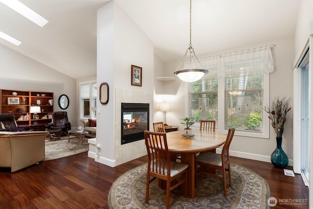 dining area featuring a tiled fireplace, a skylight, baseboards, and wood finished floors