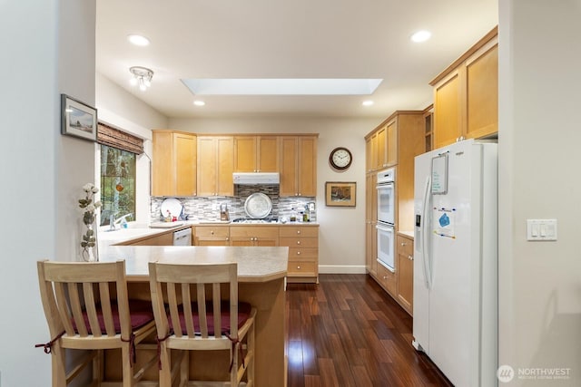 kitchen with white appliances, a peninsula, a skylight, light countertops, and under cabinet range hood