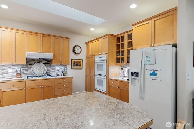 kitchen featuring white appliances, ventilation hood, a skylight, light countertops, and backsplash