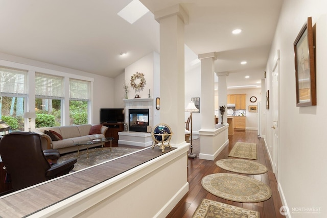 living area with a tiled fireplace, hardwood / wood-style floors, recessed lighting, decorative columns, and lofted ceiling