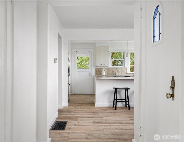 hallway featuring visible vents, light wood-type flooring, and baseboards