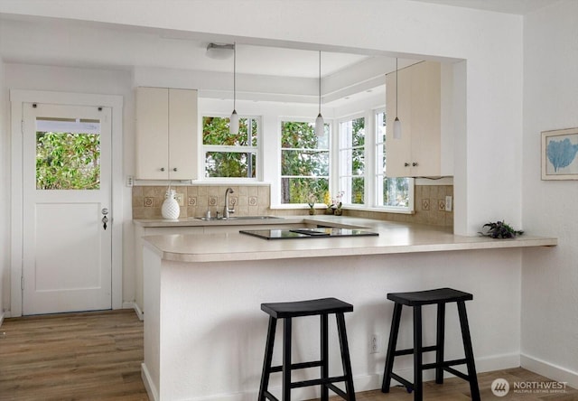 kitchen featuring wood finished floors, a peninsula, a sink, light countertops, and backsplash