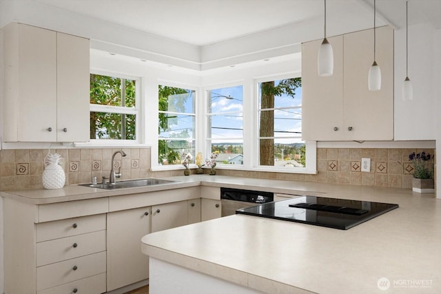 kitchen featuring a sink, light countertops, dishwasher, black electric cooktop, and tasteful backsplash