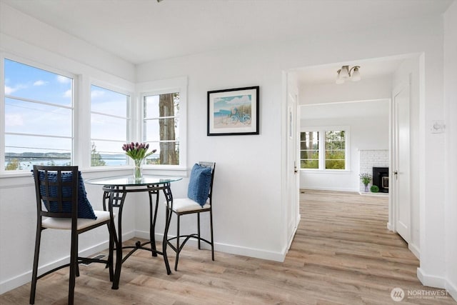 dining area featuring baseboards, light wood-style floors, and a brick fireplace