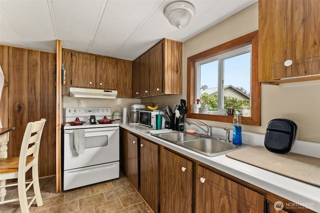 kitchen featuring white electric range, brown cabinets, under cabinet range hood, and a sink