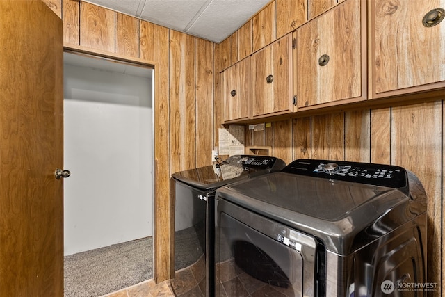 clothes washing area with cabinet space, separate washer and dryer, and wood walls