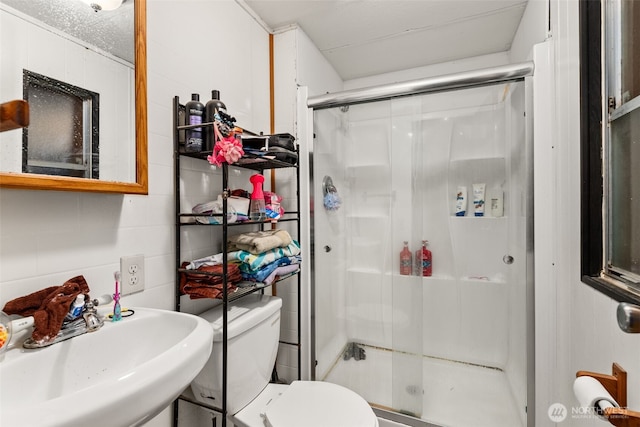 bathroom featuring a shower stall, concrete block wall, toilet, and a sink