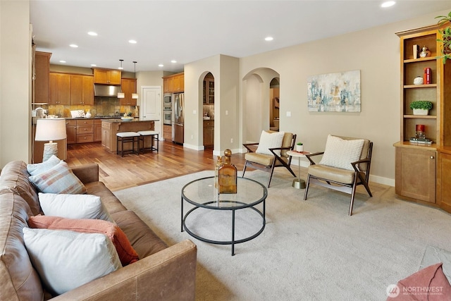 living room featuring light wood-type flooring, recessed lighting, arched walkways, and baseboards