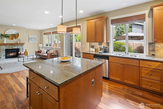 kitchen featuring dishwasher, a sink, a fireplace, dark wood-style floors, and a kitchen island