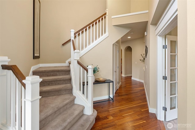 stairs featuring arched walkways, wood finished floors, baseboards, and recessed lighting