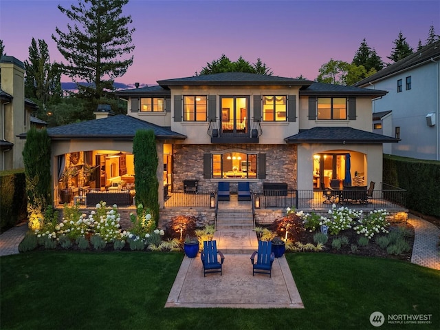 back of property at dusk with stone siding, a lawn, a patio, and stucco siding