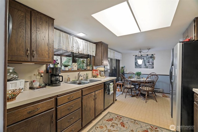 kitchen featuring light countertops, black dishwasher, a skylight, freestanding refrigerator, and a sink