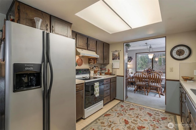 kitchen with range with electric cooktop, stainless steel refrigerator with ice dispenser, under cabinet range hood, dark brown cabinetry, and light countertops