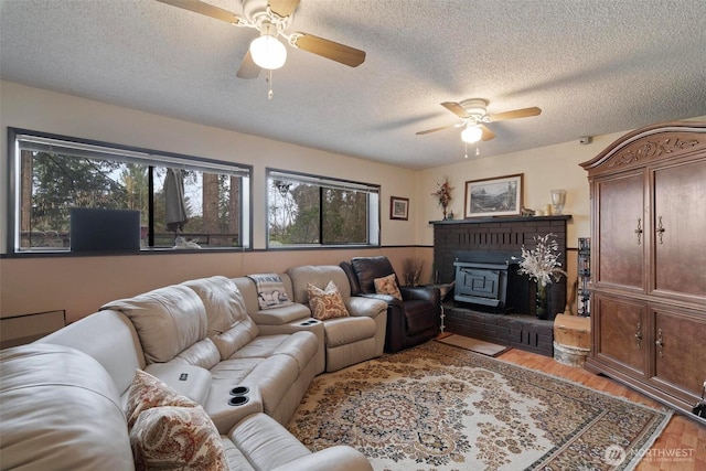 living area with a textured ceiling, a wood stove, ceiling fan, and wood finished floors