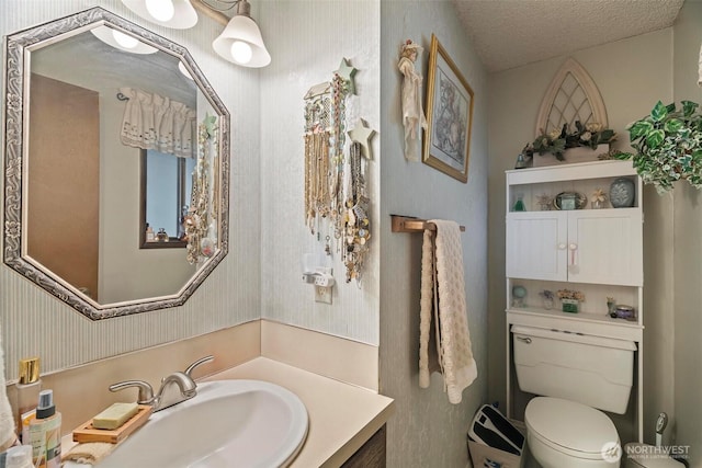 bathroom featuring vanity, toilet, wallpapered walls, and a textured ceiling