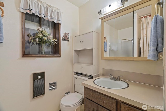 bathroom featuring heating unit, toilet, and vanity