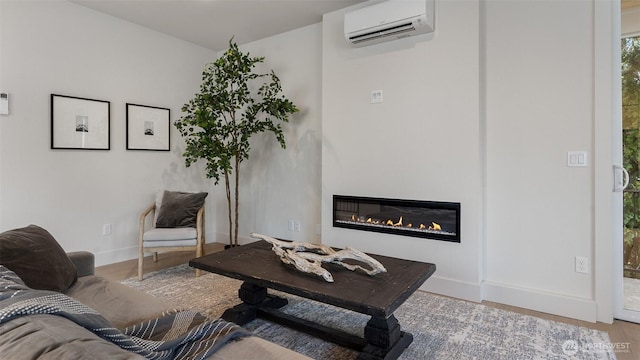 living room featuring a glass covered fireplace, baseboards, a wall unit AC, and wood finished floors