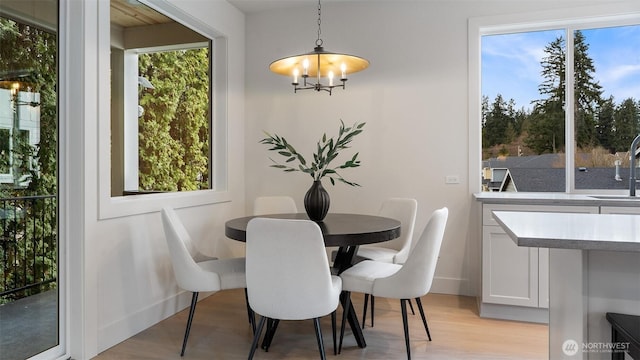 dining room with light wood-type flooring, baseboards, a notable chandelier, and a healthy amount of sunlight