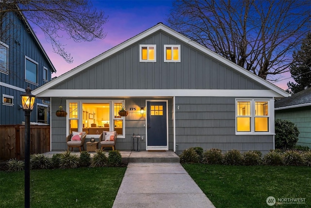 view of front of property featuring a yard, board and batten siding, covered porch, and fence