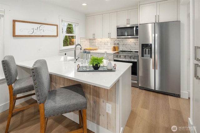 kitchen with a kitchen bar, light wood-style flooring, a sink, backsplash, and appliances with stainless steel finishes