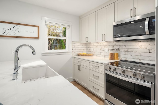 kitchen with backsplash, light wood-style flooring, white cabinets, stainless steel appliances, and a sink