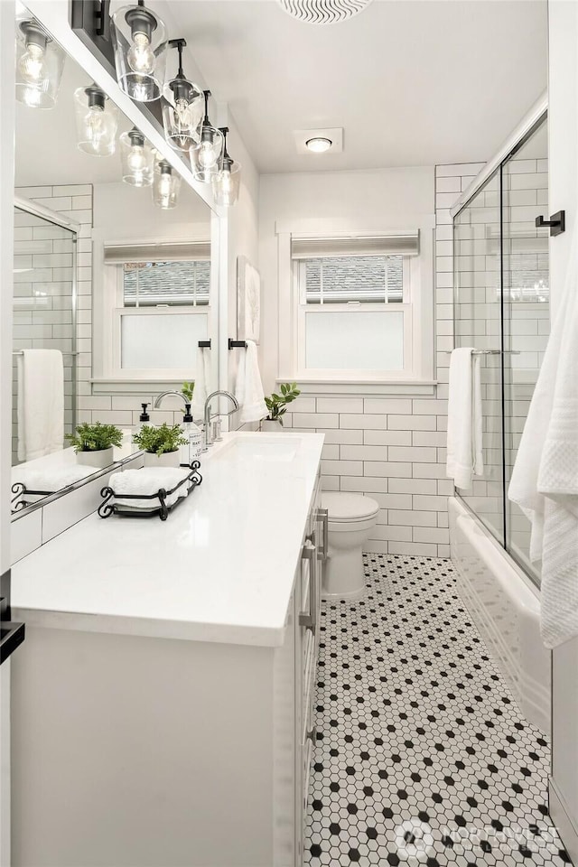 full bathroom with vanity, tile patterned flooring, tile walls, toilet, and combined bath / shower with glass door