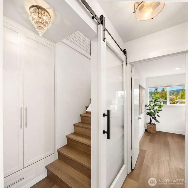 stairway with a barn door, baseboards, and wood finished floors