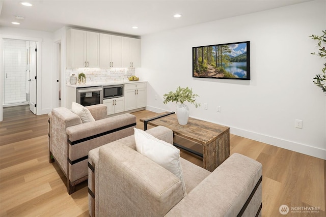 living area with baseboards, beverage cooler, recessed lighting, wet bar, and light wood-style floors